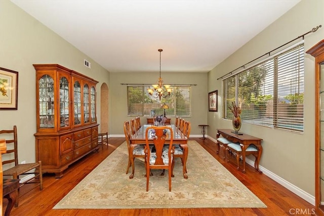 dining room featuring a chandelier, arched walkways, wood finished floors, and baseboards