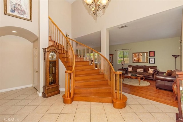 staircase with tile patterned flooring, a towering ceiling, arched walkways, a chandelier, and baseboards