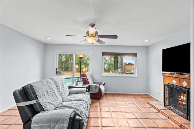 living room featuring recessed lighting, a warm lit fireplace, light tile patterned flooring, and ceiling fan