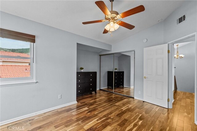 unfurnished bedroom with wood finished floors, a closet, baseboards, lofted ceiling, and visible vents