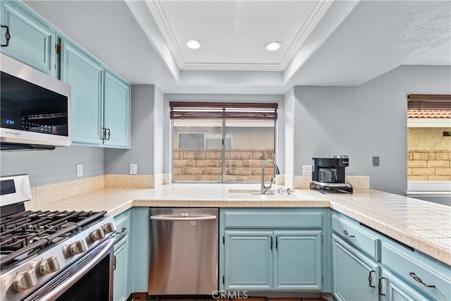 kitchen featuring recessed lighting, stainless steel appliances, a raised ceiling, blue cabinets, and a sink