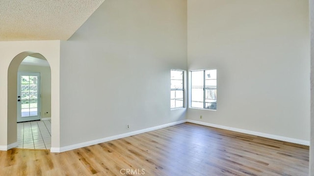 45299 Esmerado Ct, Temecula, CA 92592 - empty room with light wood-type flooring, arched walkways, baseboards, a textured ceiling, and a towering ceiling
