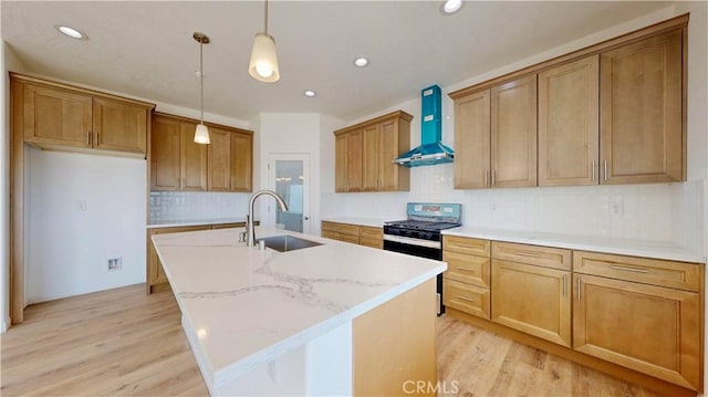 kitchen with light wood-style floors, wall chimney range hood, gas range, and a sink