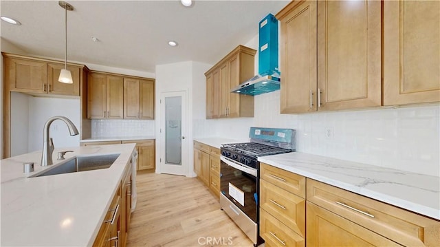 kitchen with wall chimney range hood, tasteful backsplash, a sink, light wood-type flooring, and gas range