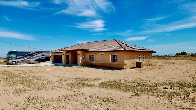 rear view of house featuring roof mounted solar panels, a tiled roof, stucco siding, an attached garage, and driveway
