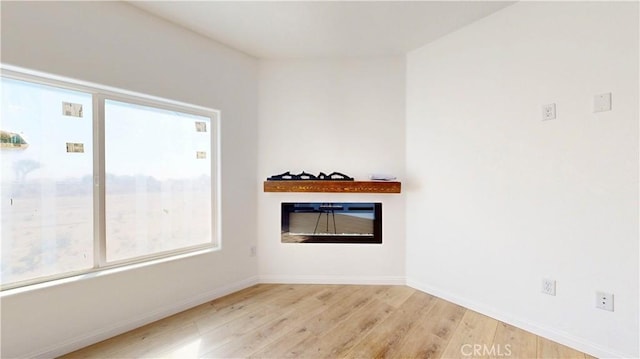 spare room with baseboards, a glass covered fireplace, and wood finished floors