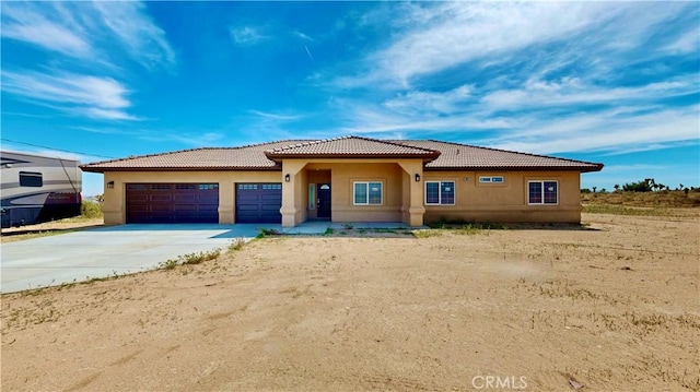 prairie-style home with stucco siding, a tile roof, a garage, and concrete driveway