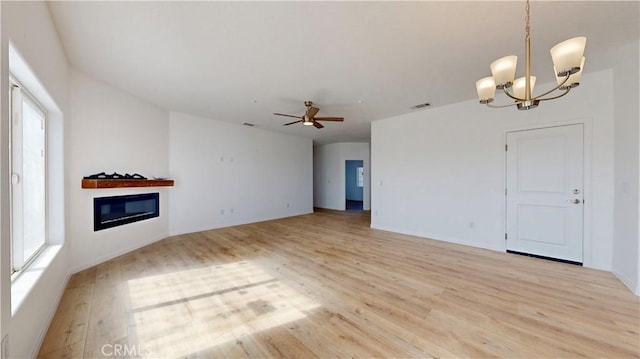 unfurnished living room featuring plenty of natural light, a glass covered fireplace, ceiling fan with notable chandelier, and light wood-type flooring