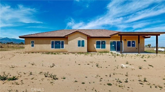 rear view of property featuring stucco siding, a tile roof, and a patio