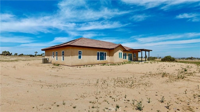 rear view of house featuring central AC, a tiled roof, and stucco siding