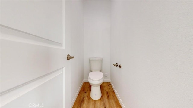bathroom featuring baseboards, wood finished floors, and toilet