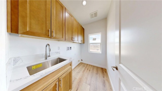 laundry area with hookup for a washing machine, a sink, light wood-style floors, cabinet space, and baseboards