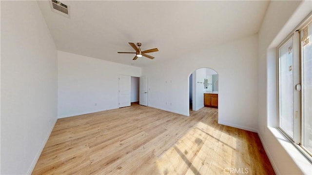 unfurnished bedroom with arched walkways, light wood-style floors, visible vents, and baseboards