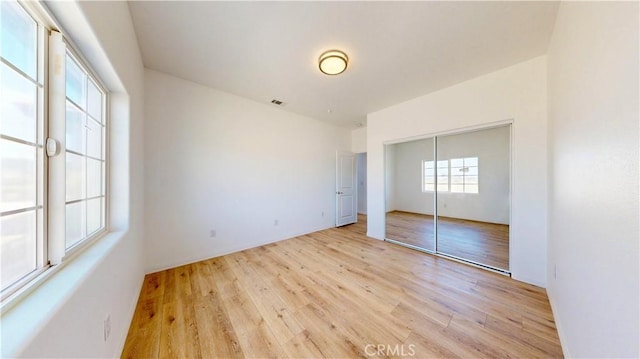 unfurnished bedroom with light wood-style flooring, a closet, and visible vents