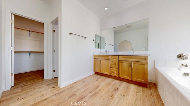 full bath featuring a bath, a walk in closet, wood finished floors, and a sink