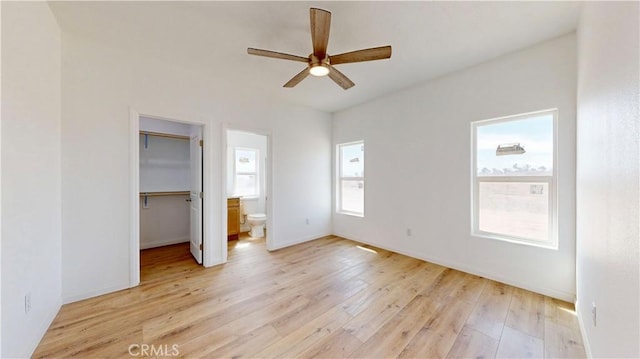 unfurnished bedroom featuring a spacious closet, a ceiling fan, light wood-type flooring, baseboards, and ensuite bathroom