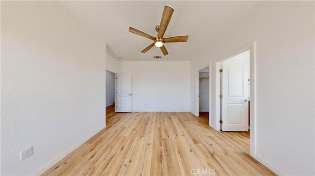 unfurnished bedroom featuring a ceiling fan, a walk in closet, a closet, baseboards, and light wood-style flooring