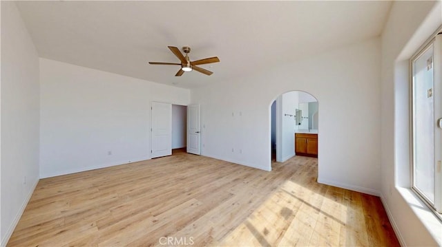 unfurnished bedroom with baseboards, arched walkways, multiple windows, and light wood-type flooring