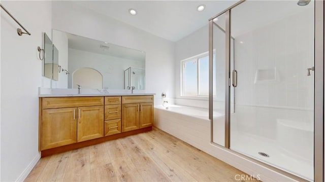 full bath with wood finished floors, double vanity, a sink, a bath, and a stall shower