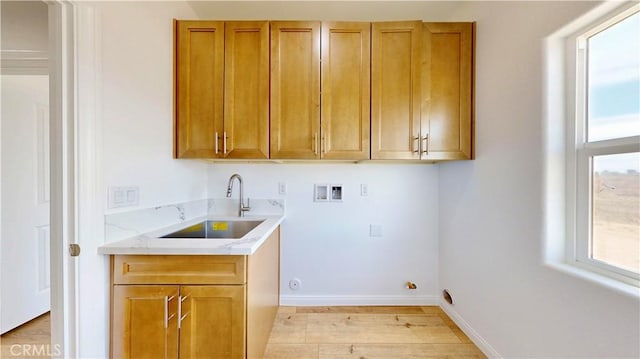 laundry area with light wood finished floors, a sink, baseboards, hookup for a washing machine, and cabinet space