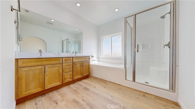 bathroom featuring double vanity, a stall shower, recessed lighting, wood finished floors, and a garden tub