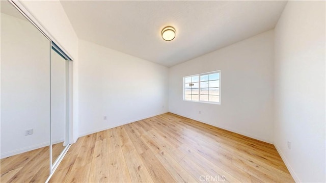 unfurnished bedroom with light wood-style flooring, a closet, and baseboards