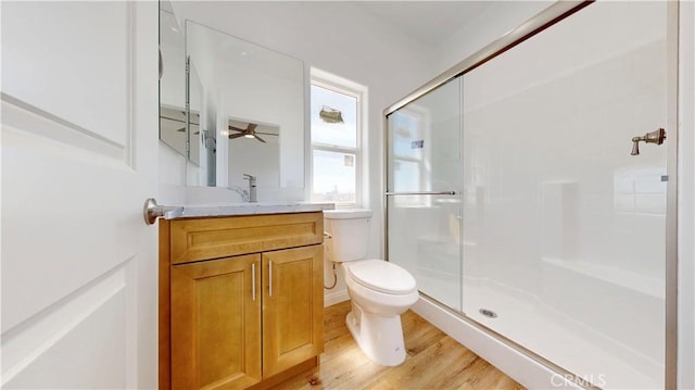 bathroom with toilet, a stall shower, wood finished floors, ceiling fan, and vanity