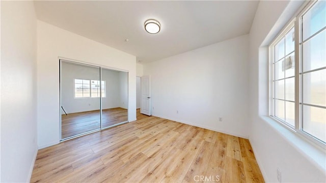 unfurnished bedroom featuring light wood-type flooring, a closet, and baseboards