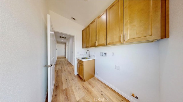 clothes washing area with hookup for a washing machine, a sink, light wood-type flooring, cabinet space, and visible vents