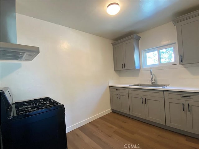 5101 Lindsey Ave, Pico Rivera, CA 90660 - kitchen featuring gray cabinetry, black range with gas cooktop, a sink, wall chimney range hood, and light wood-style floors