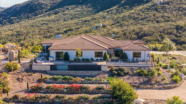 back of property featuring a wooded view, a tile roof, stucco siding, a mountain view, and fence