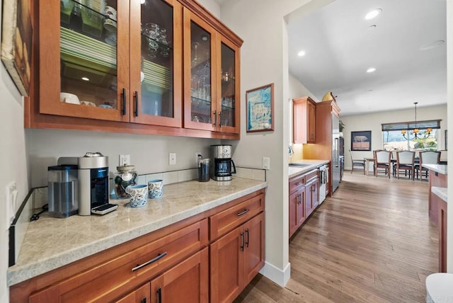 kitchen featuring brown cabinetry, wood finished floors, glass insert cabinets, and a sink