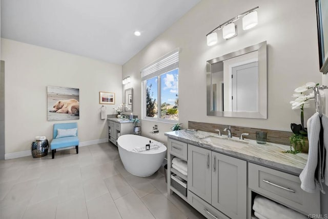 bathroom with a sink, two vanities, a freestanding bath, baseboards, and tile patterned flooring
