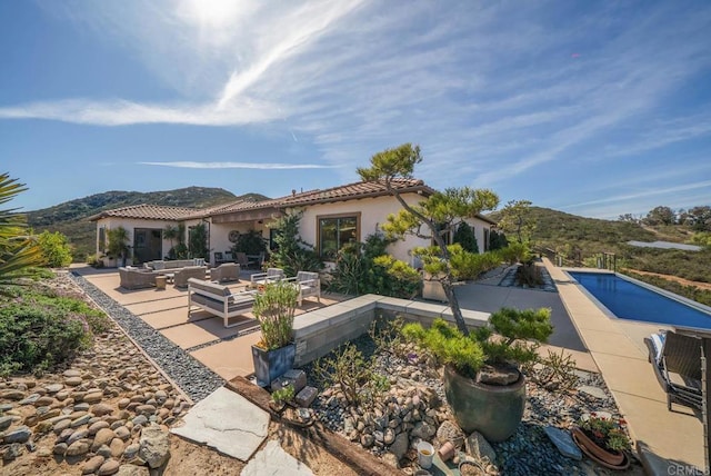 rear view of house with a patio area, an outdoor living space, a mountain view, an outdoor pool, and stucco siding
