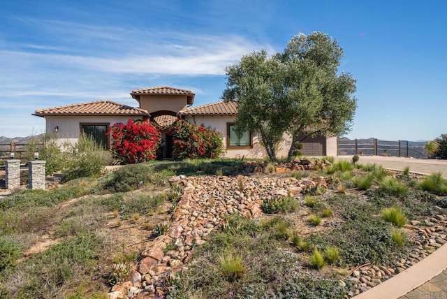 mediterranean / spanish-style house featuring stucco siding, fence, an attached garage, and a tile roof