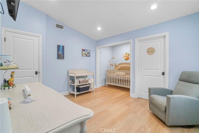 bedroom with light wood-style floors, recessed lighting, a crib, and visible vents