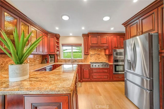 kitchen featuring tasteful backsplash, appliances with stainless steel finishes, recessed lighting, light wood finished floors, and light stone countertops