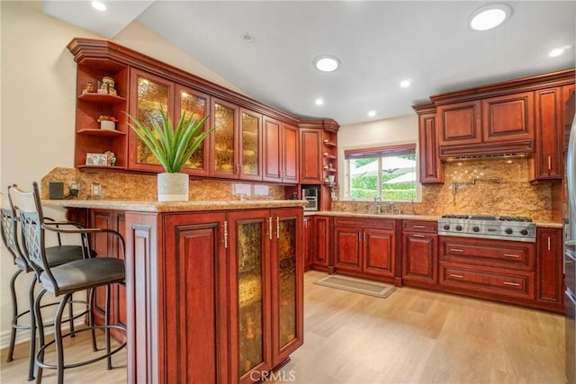 kitchen featuring a peninsula, glass insert cabinets, open shelves, light wood-style floors, and stainless steel gas cooktop