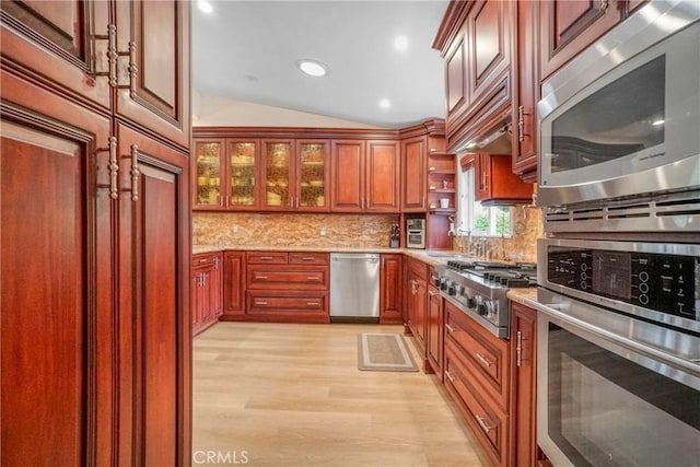 kitchen with light wood-type flooring, vaulted ceiling, light stone countertops, decorative backsplash, and stainless steel appliances