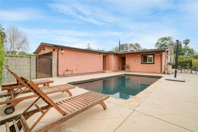 back of house featuring an outdoor pool, a patio area, stucco siding, and a gate