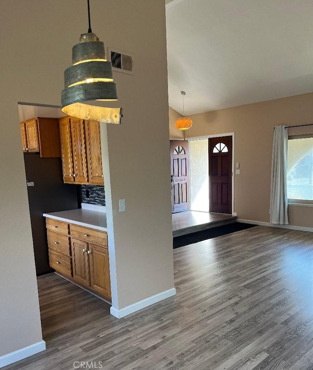 kitchen featuring dark wood-style flooring, visible vents, brown cabinetry, baseboards, and backsplash