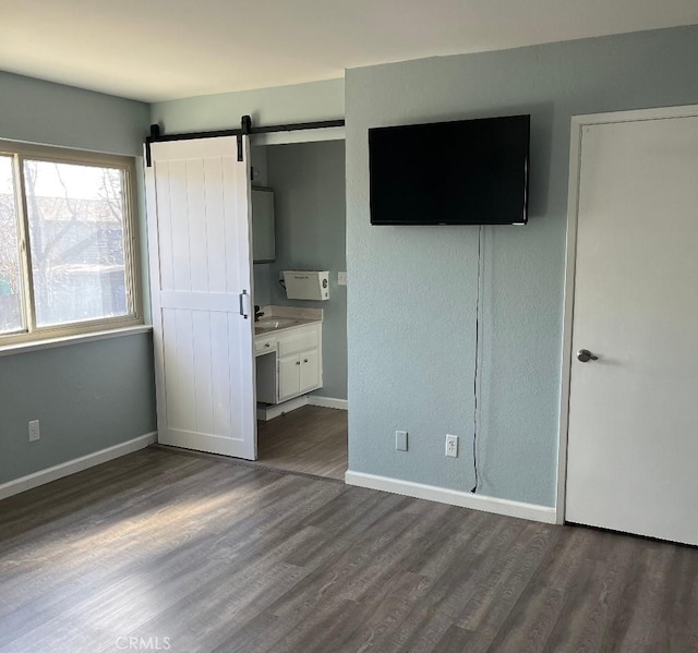unfurnished bedroom with baseboards, dark wood-style flooring, ensuite bathroom, and a barn door