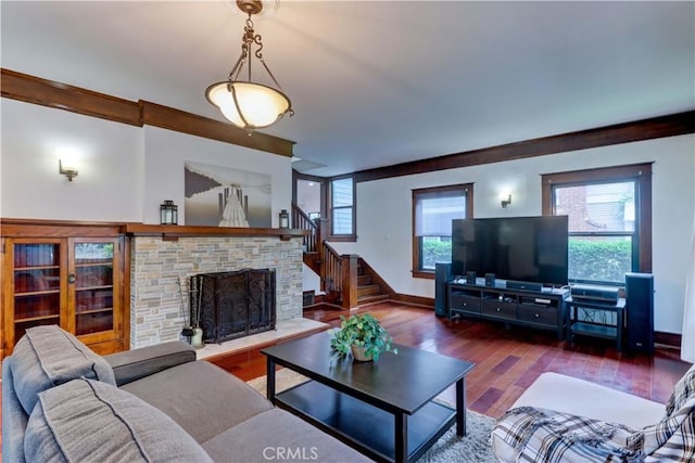 living room featuring baseboards, a fireplace with raised hearth, wood finished floors, and stairway