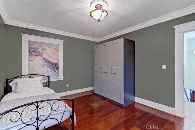 bedroom featuring baseboards, crown molding, wood finished floors, and a closet