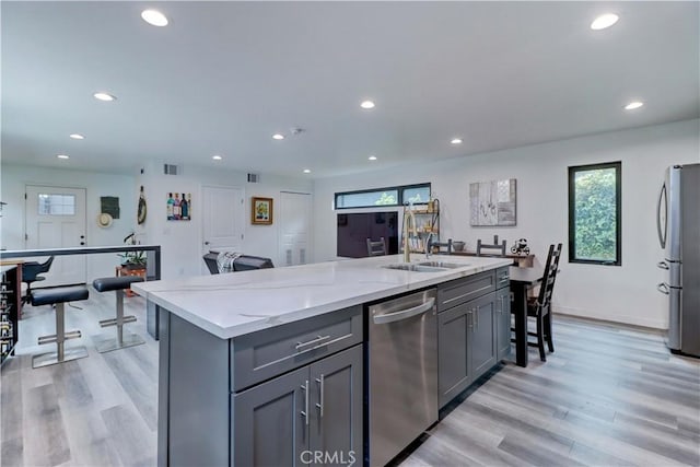 kitchen featuring light stone countertops, a sink, light wood-style flooring, gray cabinetry, and stainless steel appliances