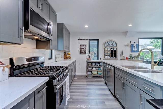 kitchen with light stone counters, a sink, gray cabinetry, and stainless steel appliances