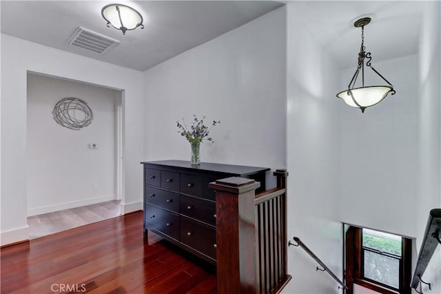 hallway featuring baseboards, visible vents, dark wood finished floors, and an upstairs landing