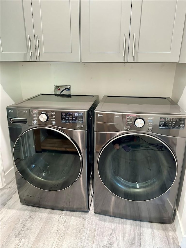 clothes washing area featuring cabinet space, separate washer and dryer, baseboards, and wood finished floors