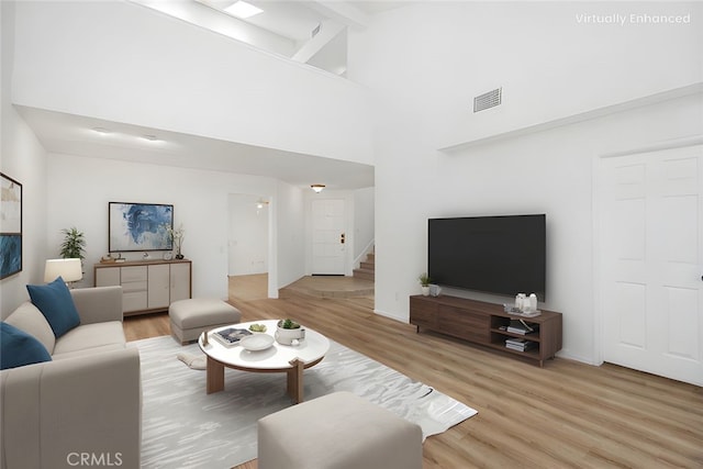 living area with beam ceiling, light wood finished floors, stairs, a towering ceiling, and visible vents