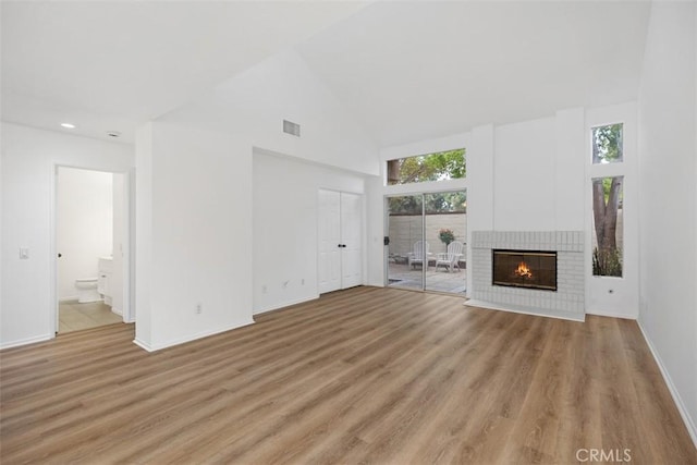 unfurnished living room with light wood finished floors, a fireplace, high vaulted ceiling, baseboards, and visible vents